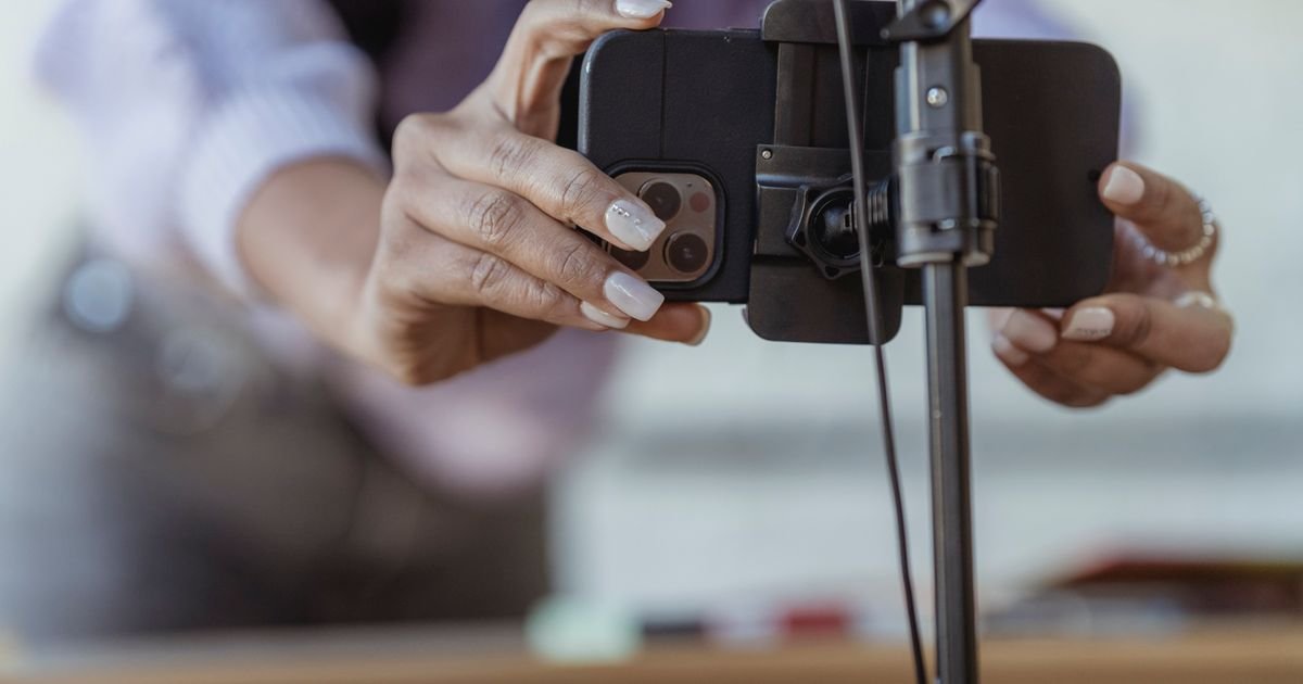 Hands clamping a smartphone into a tripod mount, set up to record a vertical video.